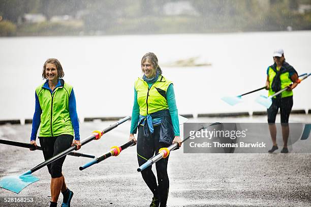 Smiling mature female rowers carrying oars in rain