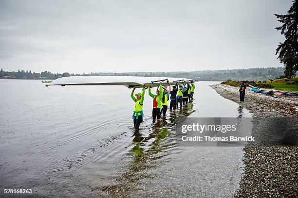 group of mature female rowers lifting rowing shell - coordinated effort stock pictures, royalty-free photos & images