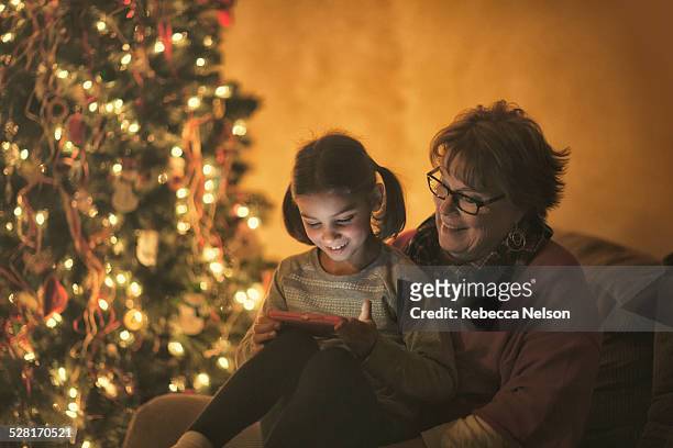 grandma and granddaughter looking at phone - christmas smartphone stock-fotos und bilder