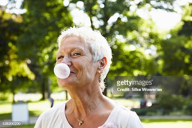 portrait of senior woman blowing a large chewing gum bubble with smile - old people having fun stock pictures, royalty-free photos & images