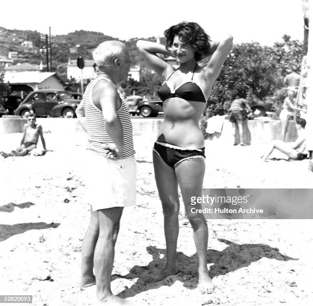 Spanish painter Pablo Picasso makes a young woman wearing a bikini smile on the beach at Golfe Juan on the Riviera, Vallauris, France, 1960s.