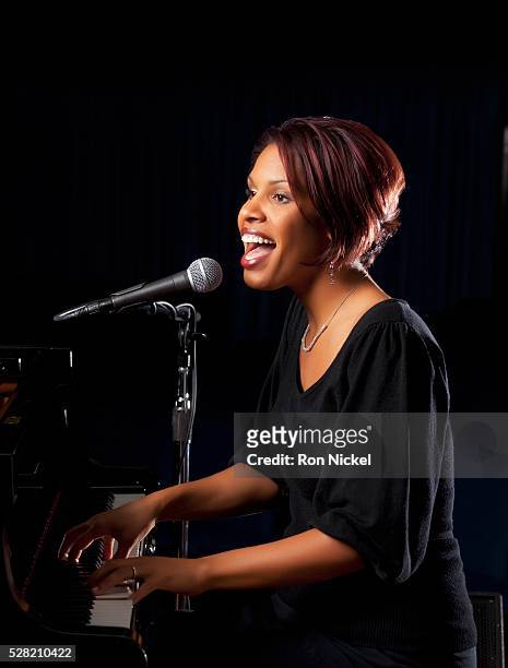 a woman playing the piano and singing into a microphone - pianist stock pictures, royalty-free photos & images