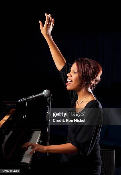 a woman playing the piano and singing in worship with her hand raised - pianist stock pictures, royalty-free photos & images