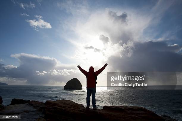silhouette of a person lifting their hands standing at cape kiwanda cliffs with a view of haystack rock - tillamook rock light stock pictures, royalty-free photos & images