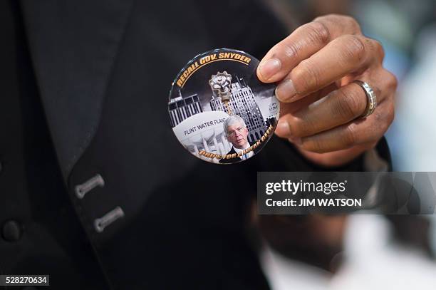 Member of the audience holds up a button calling for a recall against Michigan Governor Rick Snyder as US President Barack Obama speaks at...