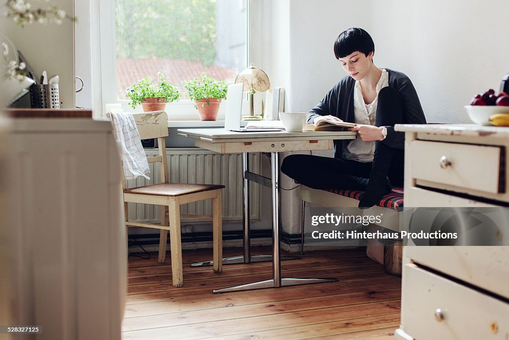 Female Student Reading A Book In Her Kitchen