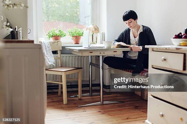female student reading a book in her kitchen - book table stockfoto's en -beelden