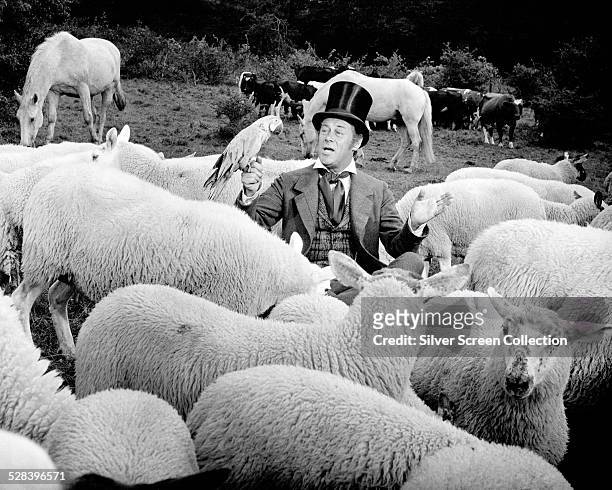 English actor Rex Harrison as Doctor John Dolittle, holding a parrot and surrounded by sheep, horses and cattle, in 'Doctor Dolittle', directed by...