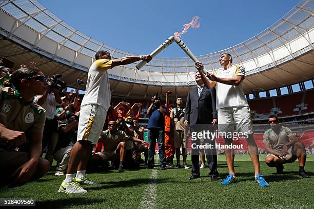 Brazilian former footballer Lucio and Brasilia's governor Rodrigo Rollemberg receive the Olympic flame from fireman Haudson Alves at the field of the...
