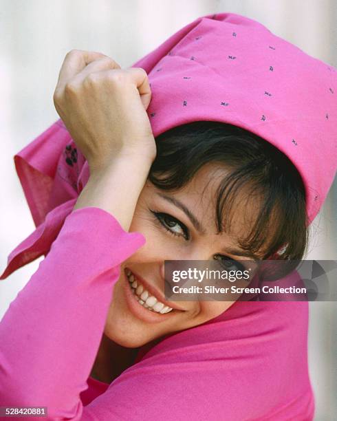 Italian actress Claudia Cardinale wearing a pink top and headscarf, circa 1965.