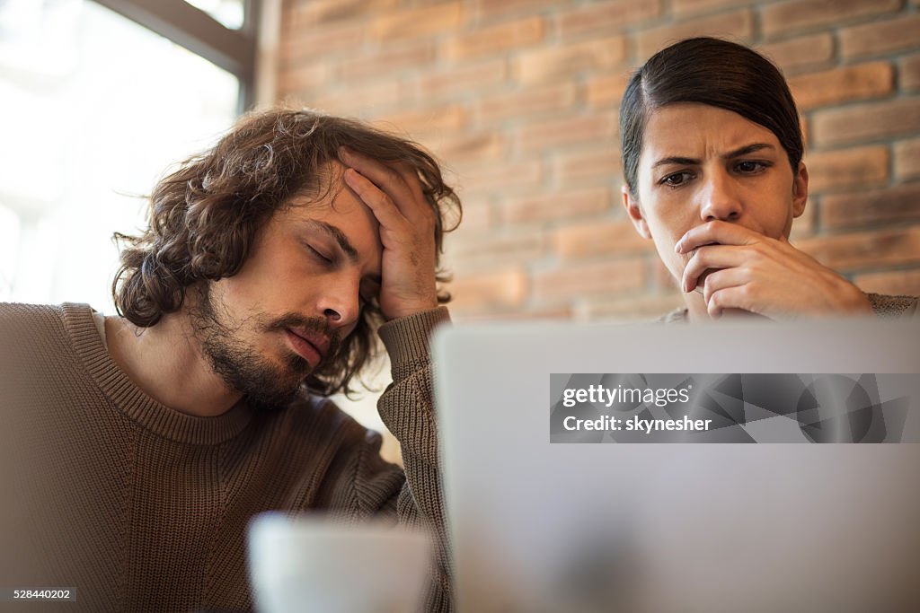 Young worried couple at home using laptop.