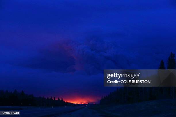 Plume of smoke hangs in the air as forest fires rage on in the distance in Fort McMurray, Alberta on May 4, 2016. Numerous vehicles can be seen...