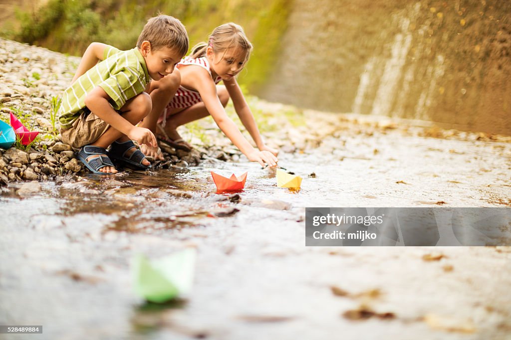 Jungen und Mädchen spielen mit Papier-Boote auf dem Fluss