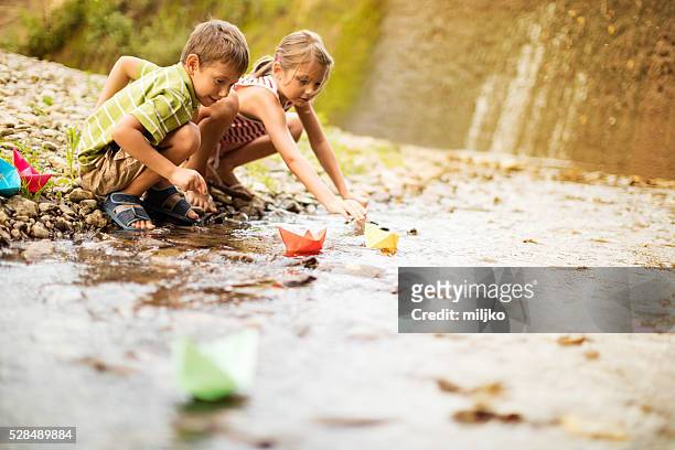 boy and girl playing paper boats on the river - paper boat stock pictures, royalty-free photos & images