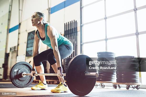 mature woman lifting weights in gym setting - weight lifting stockfoto's en -beelden