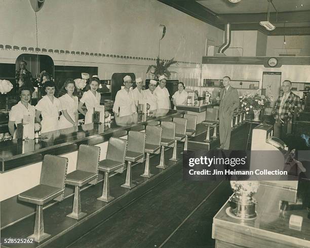 Black and white photograph of uniformed staff standing behind restaurant counter.