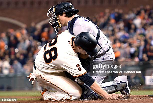 Buster Posey of the San Francisco Giants gets tagged out at home plate while colliding with catcher Tony Wolters of the Colorado Rockies in the...