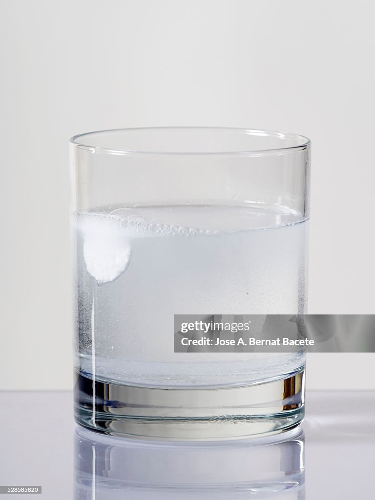 Tablet of effervescent medicine falling down inside a water glass