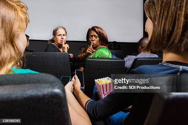 wütende frau shushing teenager mit handy in movie theater - movie still stock-fotos und bilder