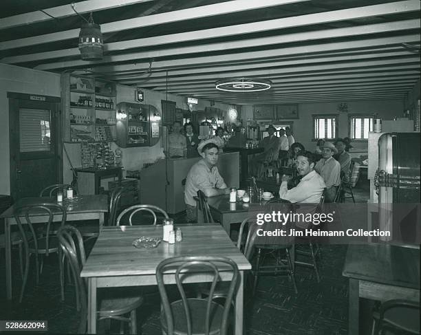 Black and white photograph featuring patrons sitting at tables and staff standing in background.