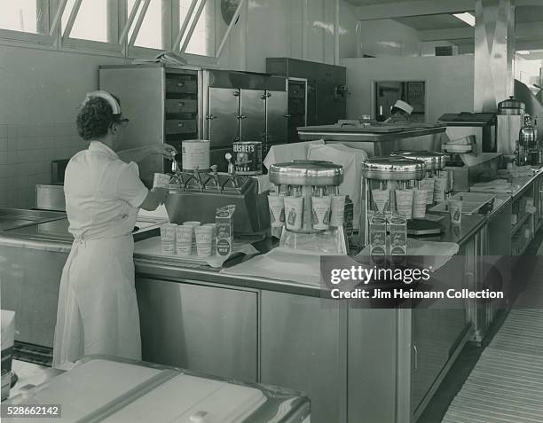 Black and white photograph of waitress serving drink from soda fountain.