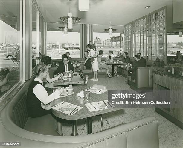 Black and white photograph of diners sitting at tables in restaurant with large picture windows.