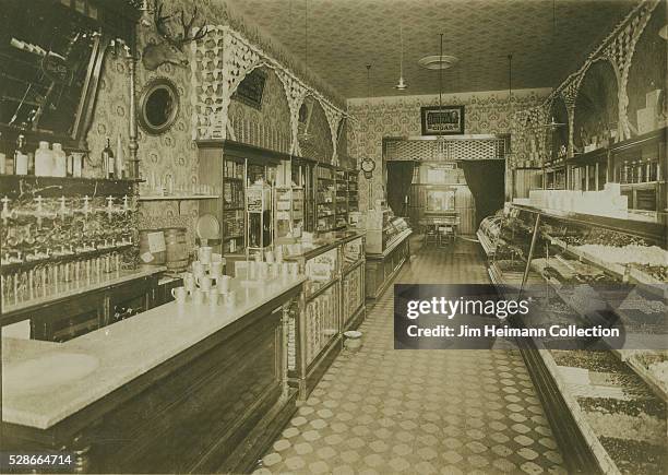 Black and white photograph of empty counter with glass display cabinet, taxidermy on walls and ornate decor.