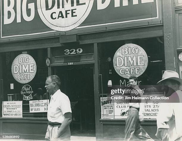 Black and white photograph featuring men passing in front of Big Dime Cafe.