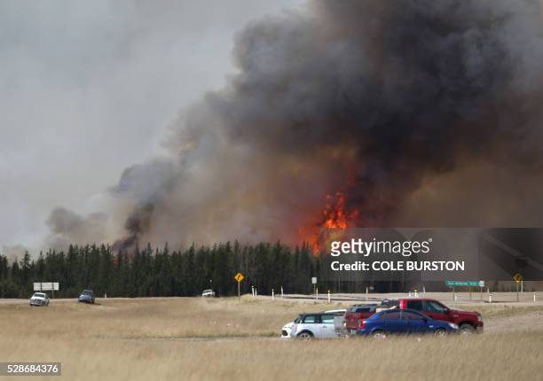 Convoy of evacuees drives south as flames and smoke rises along the highway near near Fort McMurray, Alberta on May 6, 2016. - Canadian police led...