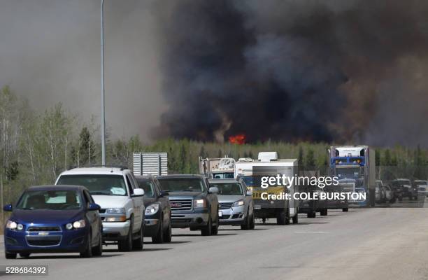Convoy of evacuees drives south as flames and smoke rises along the highway near near Fort McMurray, Alberta on May 6, 2016. - Canadian police led...