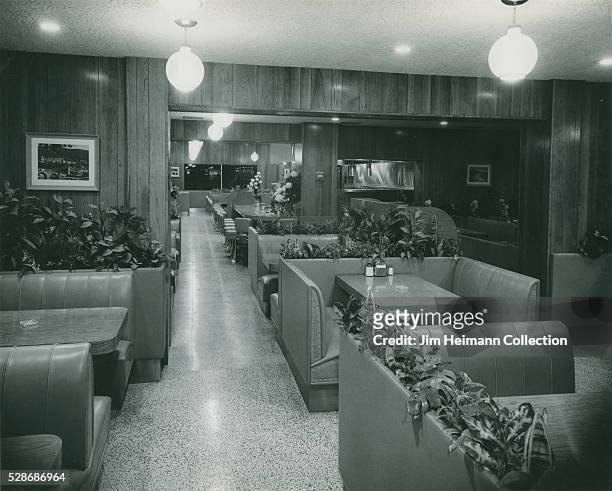 Black and white photograph featuring booths, plants, and wood paneled walls.