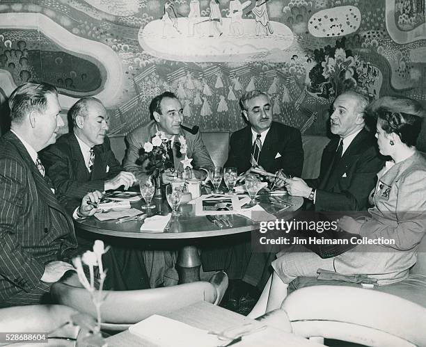 Black and white photograph of people sitting at round booth in restaurant.