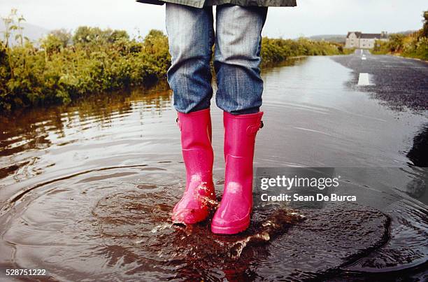 woman in rubber boots standing on street in puddle - rubberlaars stockfoto's en -beelden