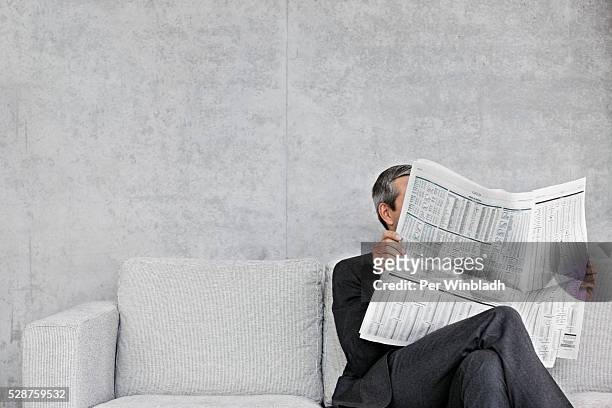 man reading newspaper on sofa - blätter stock-fotos und bilder