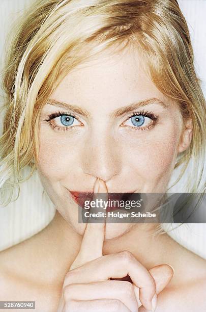 young blond woman holding finger to her mouth - stilte stockfoto's en -beelden