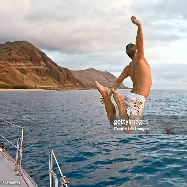 young man jumping from boat into water - iris mann stock-fotos und bilder