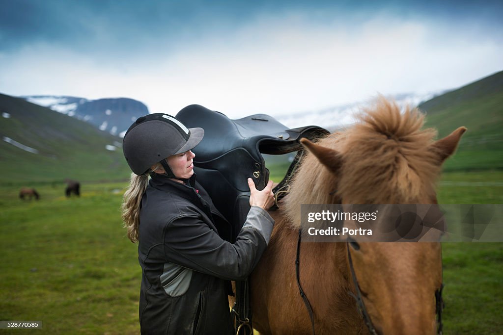 Woman keeping saddle on horse at field