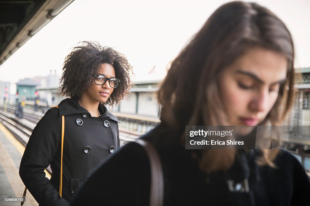 Two women waiting on an above-ground platform for the arriving subway train