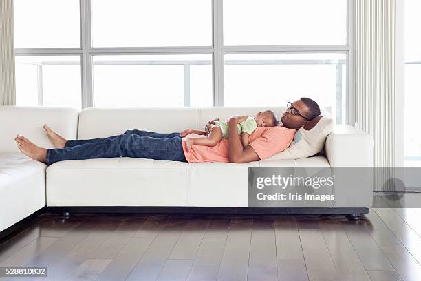 father and son (6-12 months) relaxing on sofa - iris family stock-fotos und bilder