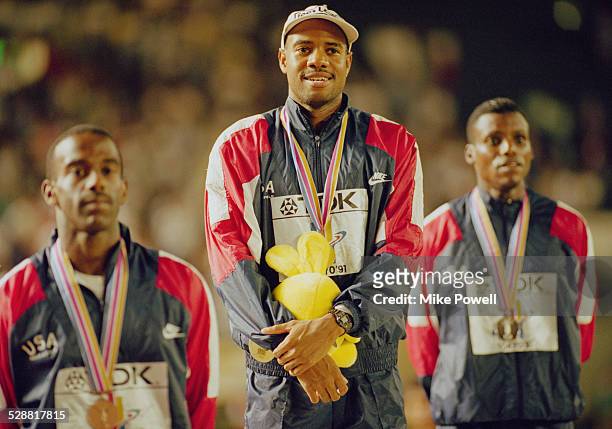Mike Powell of the United State celebrates on the podium with silver medallist Carl Lewis and bronze medallist Larry Myricks after making his world...