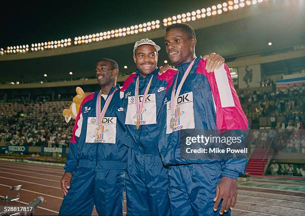Mike Powell of the United State celebrates on the podium with silver medallist Carl Lewis and bronze medallist Larry Myricks after making his world...