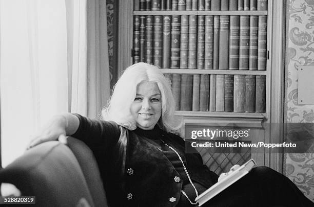 English actress Diana Dors pictured sitting on a chair in a library in London on 14th February 1978.