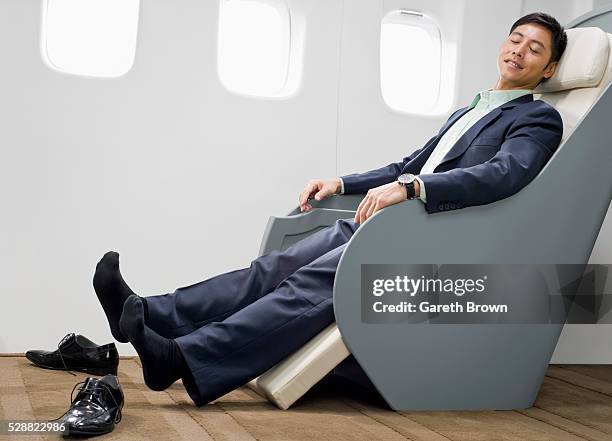 businessman relaxing on reclining chair on airplane - recostarse fotografías e imágenes de stock
