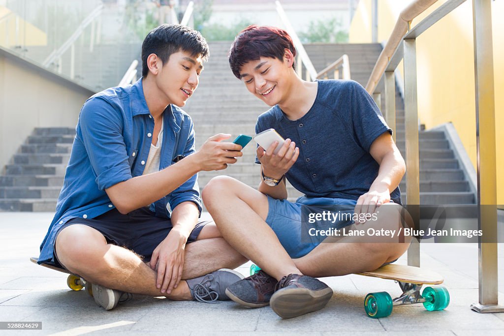 Young men sitting on skateboards looking at smart phones