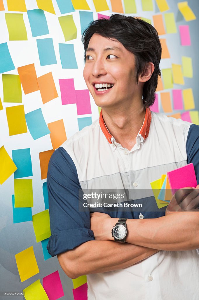 Young man smiling in front of glass wall covered in colorful sticky notes