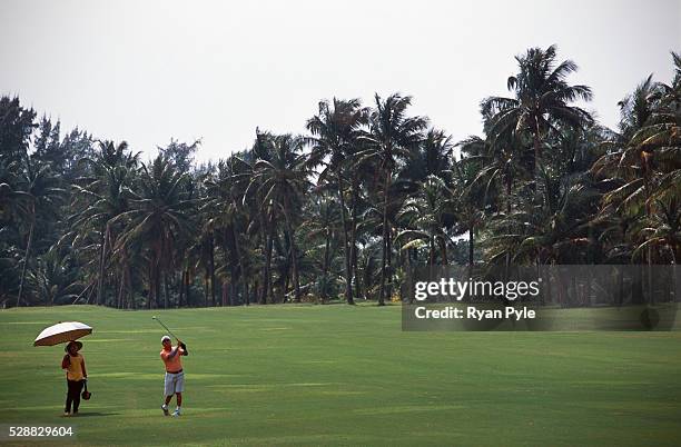 Caddy holds an umbrella as a golfer watching his approach shot at the Taida Golf Course just outside Haikou city, the capital of Hainan province in...