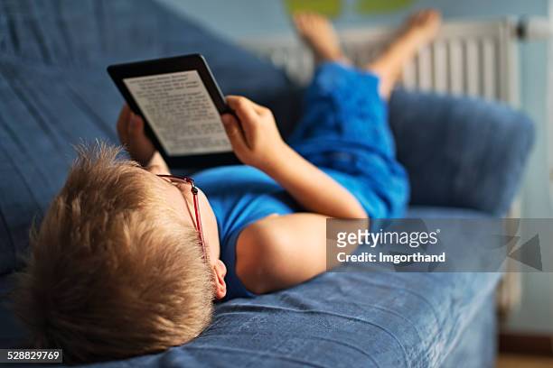 kleiner junge liest ein ebook auf couch - e reader stock-fotos und bilder