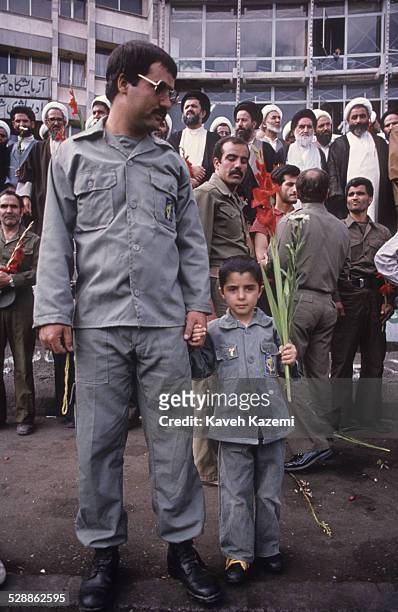 During the Iran-Iraq War, an Iranian Revolutionary Guard holds the hand of his son also dressed in military fatigue on Pasdaran's Day, commemorating...