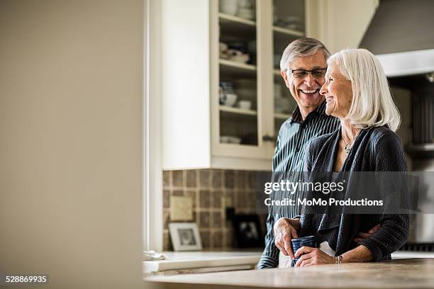 senior couple laughing in kitchen - financial freedom stock pictures, royalty-free photos & images