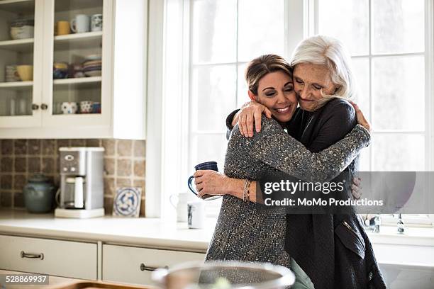 mother and daughter hugging in kitchen - senior adult bildbanksfoton och bilder